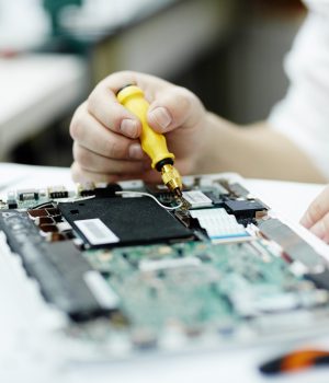 Closeup shot of unrecognizable man assembling circuit board in laptop using screwdriver and different tools on table in workshop